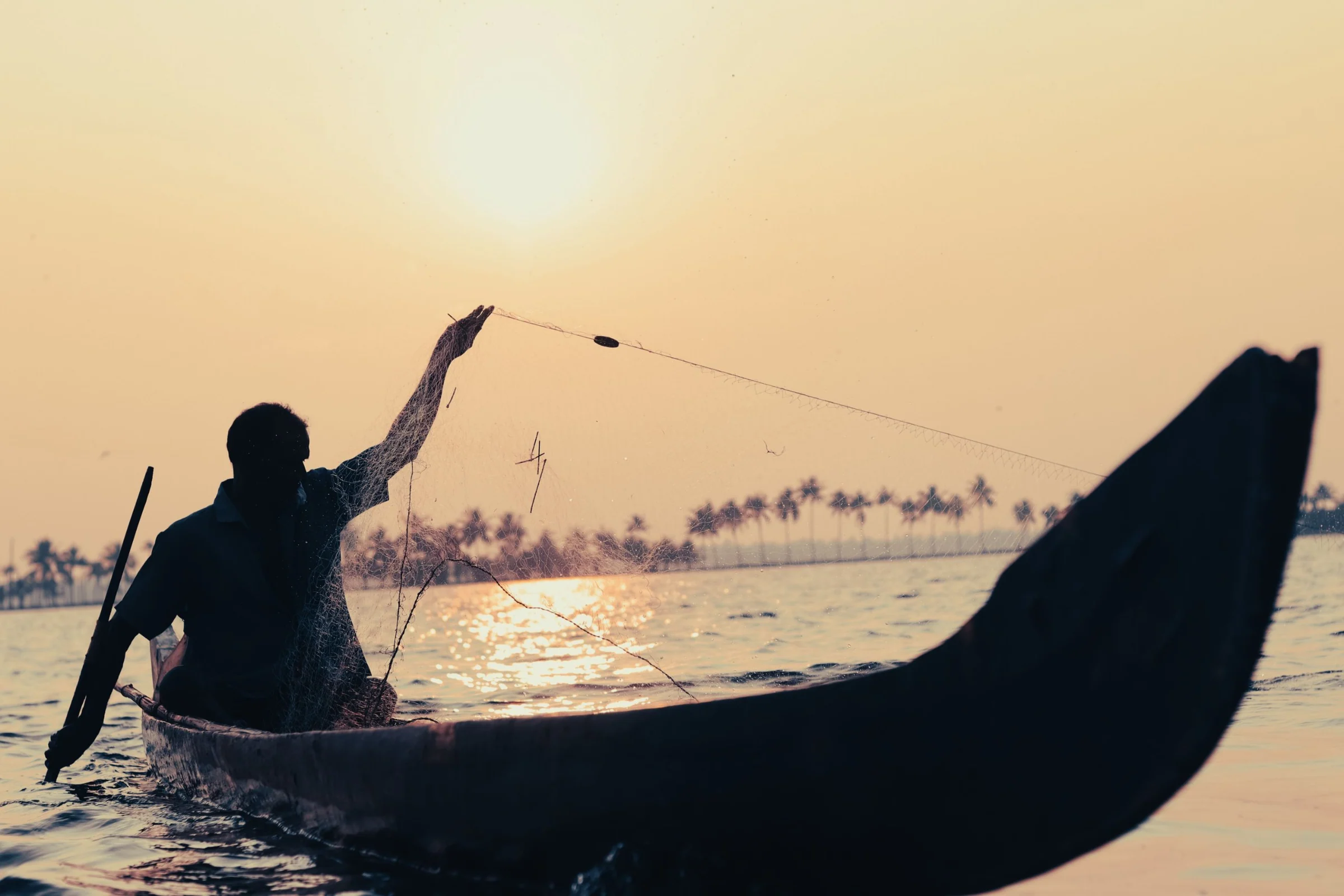 Ein Fischer wirft bei Sonnenuntergang sein Netz von einem Kanu auf den Backwaters aus